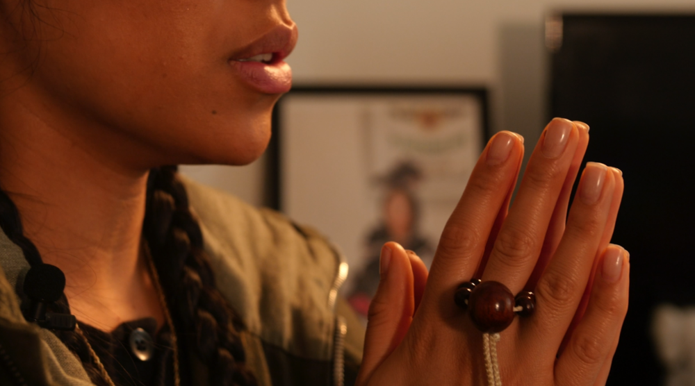 Stylist Aleali May with her palms pressed together chanting Nam-myoho-renge-kyo with prayer beads in her hand