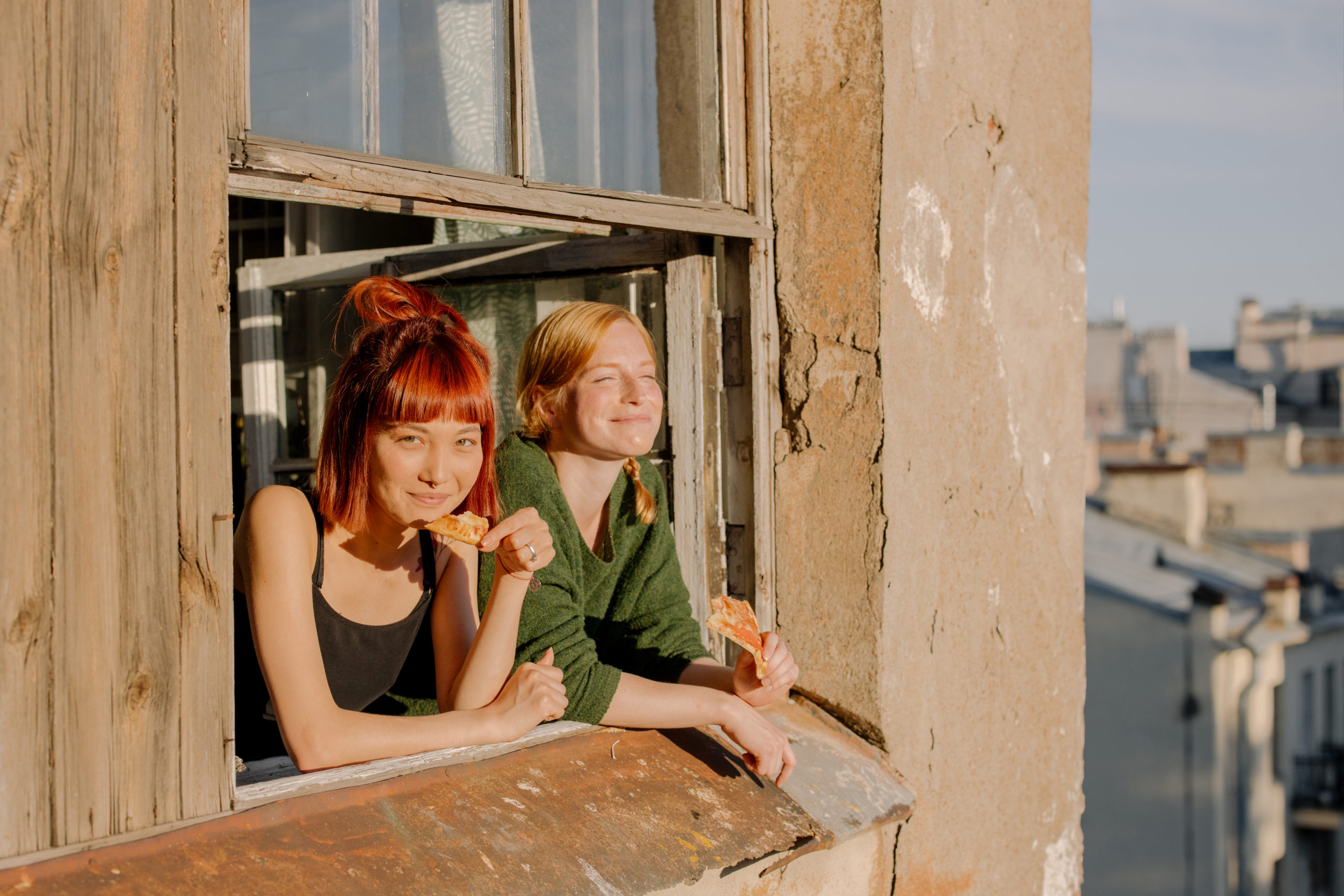 Two girls looking out their window and smiling while eating pizza