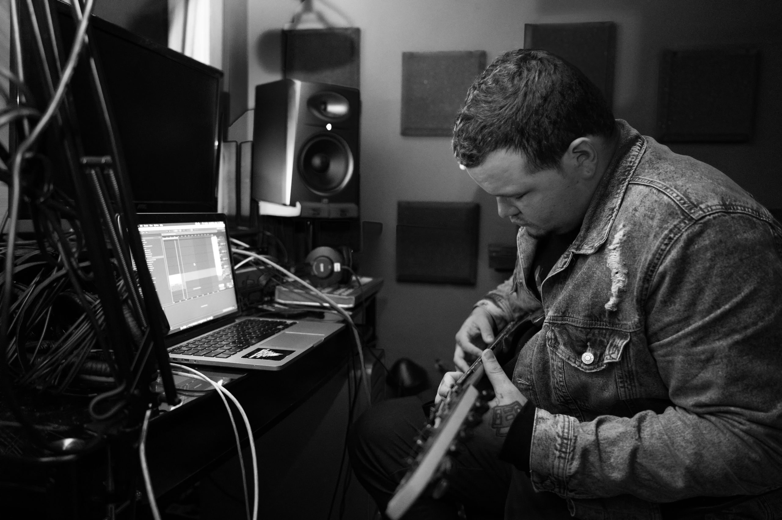 A guy in a black and white image in a recording studio playing the guitar