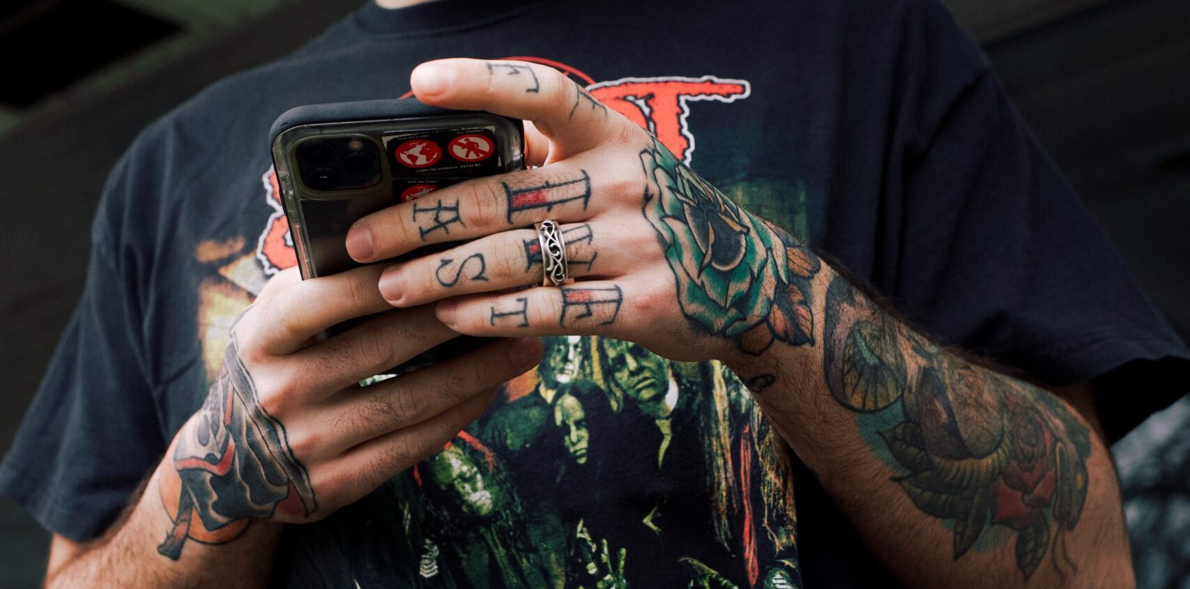 Guy looking at his phone with tattoos, wearing a bright yellow NY baseball cap