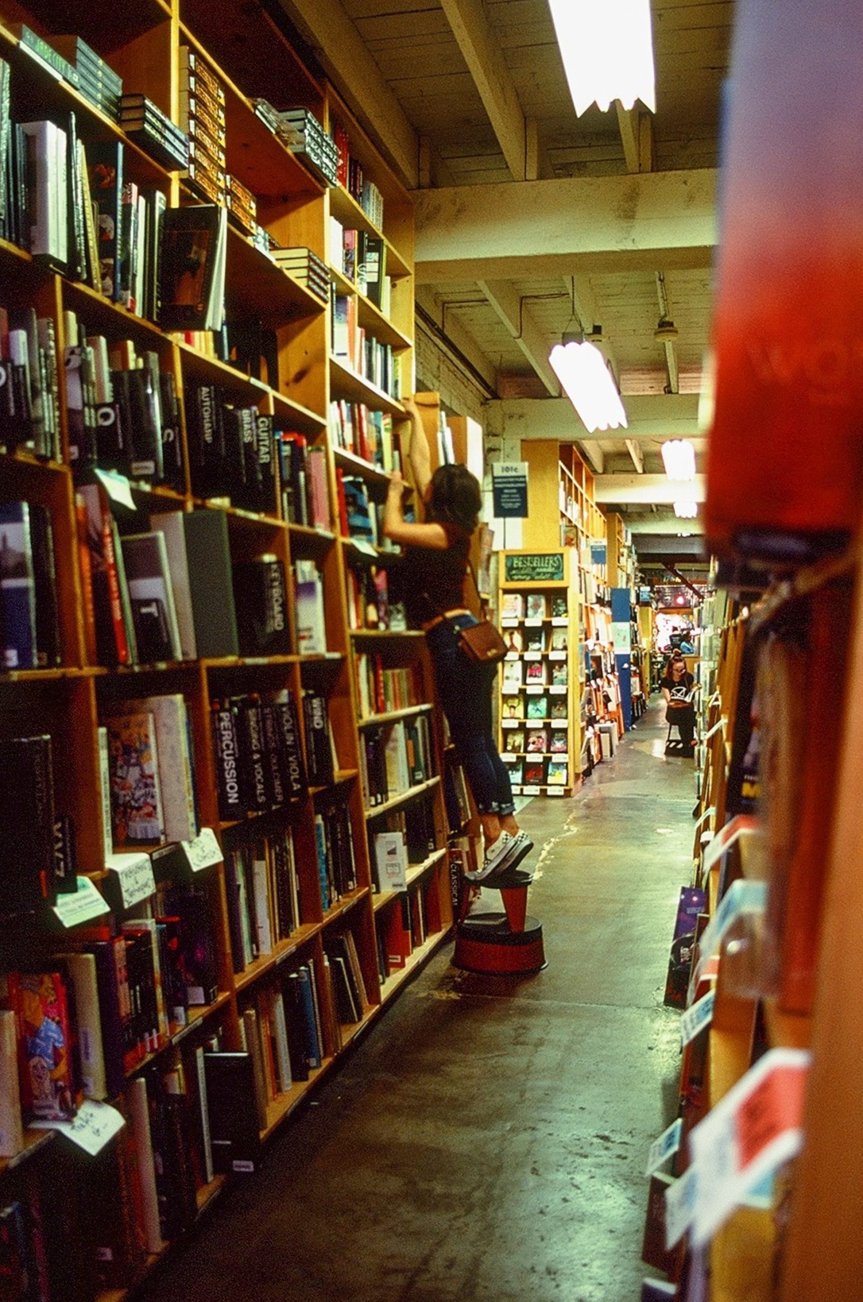 Girl standing on a ladder reaching for a book in a bookstore